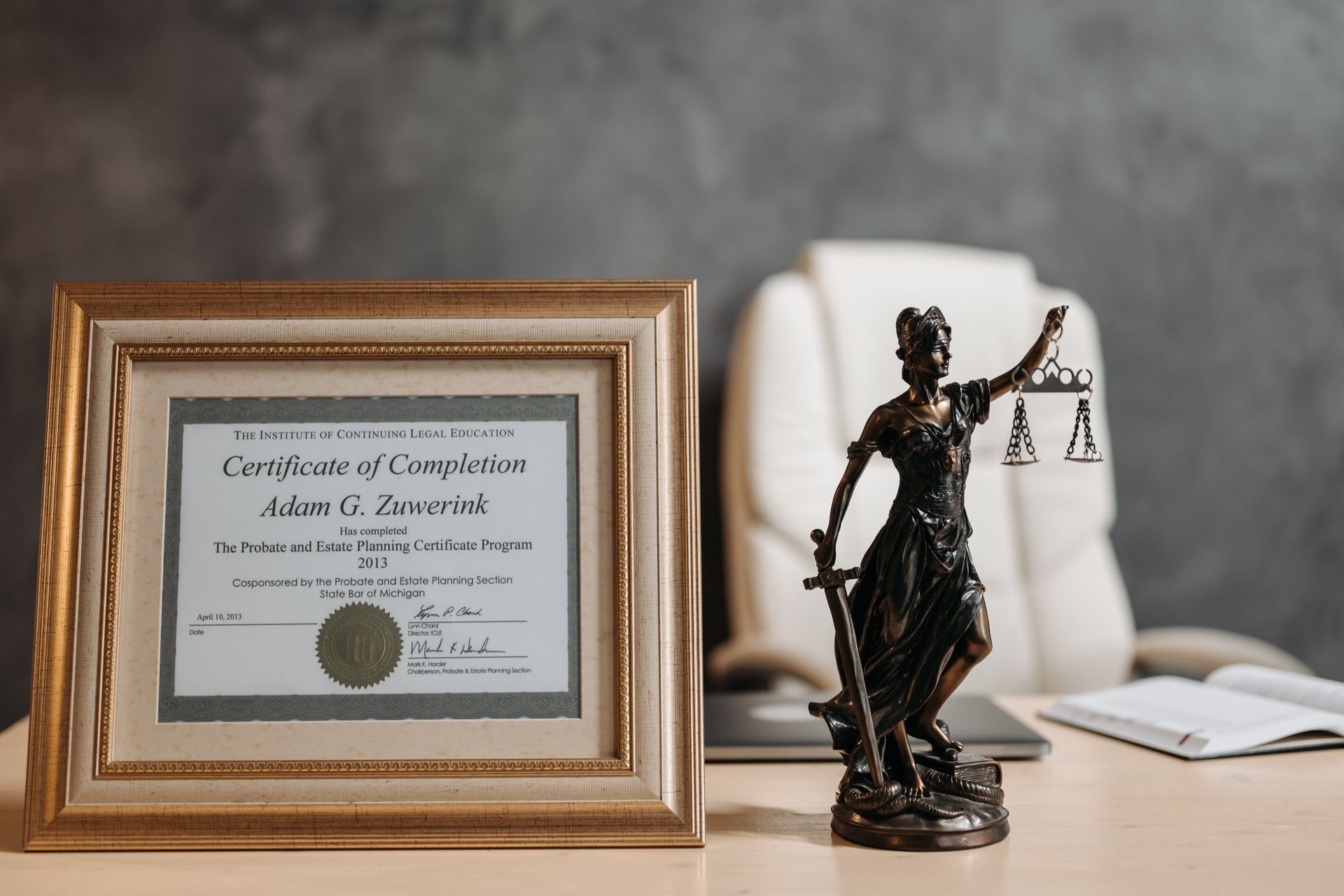 Lady Justice figurine beside a framed legal certificate